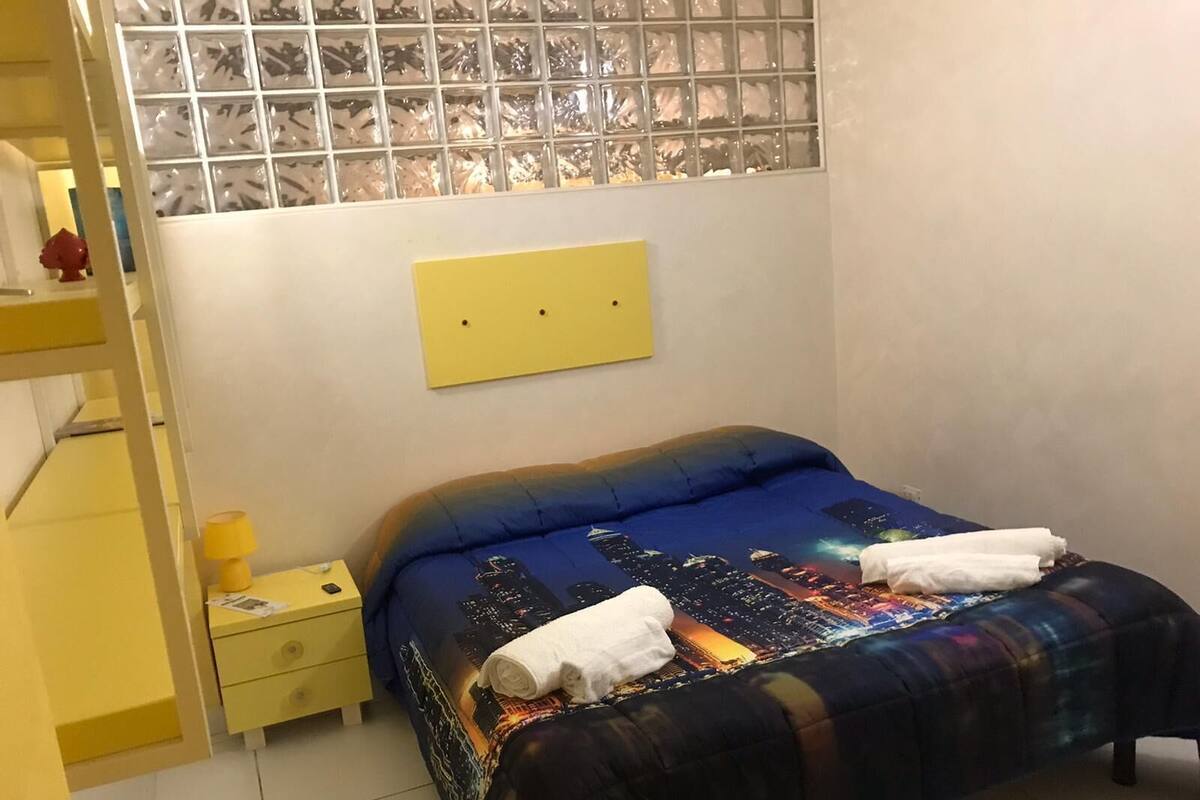 Une chambre à coucher avec un lit, une table de chevet, un mur jaune et une fenêtre à vitres dépolies.