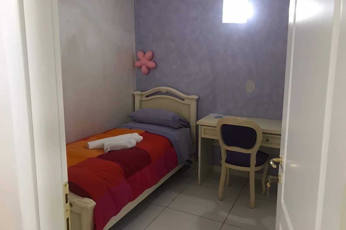 Une petite chambre à coucher, bien rangée, avec un lit, un bureau et une chaise.