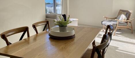 Un comedor con una mesa de madera, cuatro sillas, una planta en maceta y vistas del exterior a través de un gran ventanal.