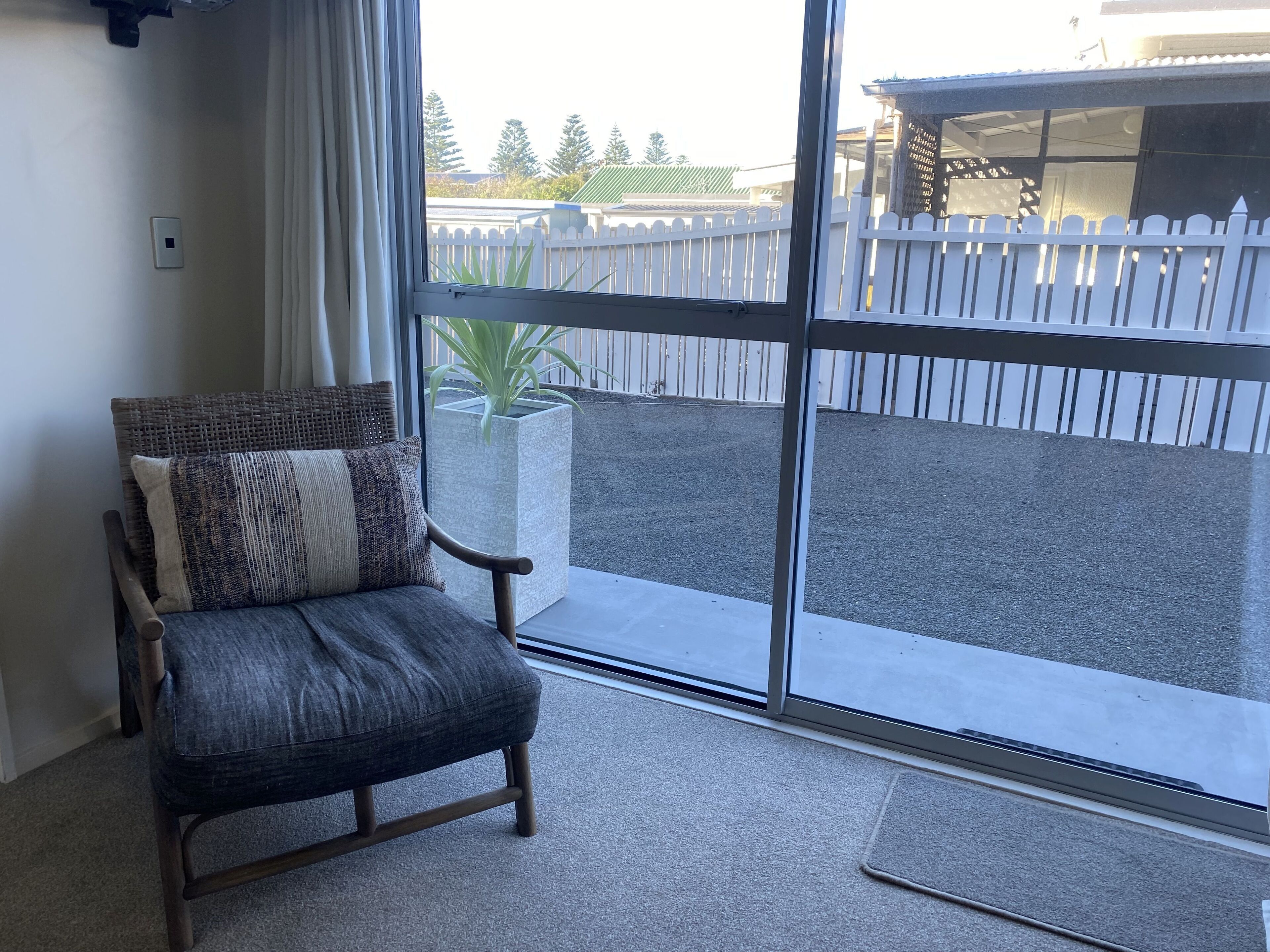 A room with a large sliding glass door leading to an outdoor area with a white fence and trees.