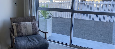 A room with a large sliding glass door leading to an outdoor area with a white fence and trees.