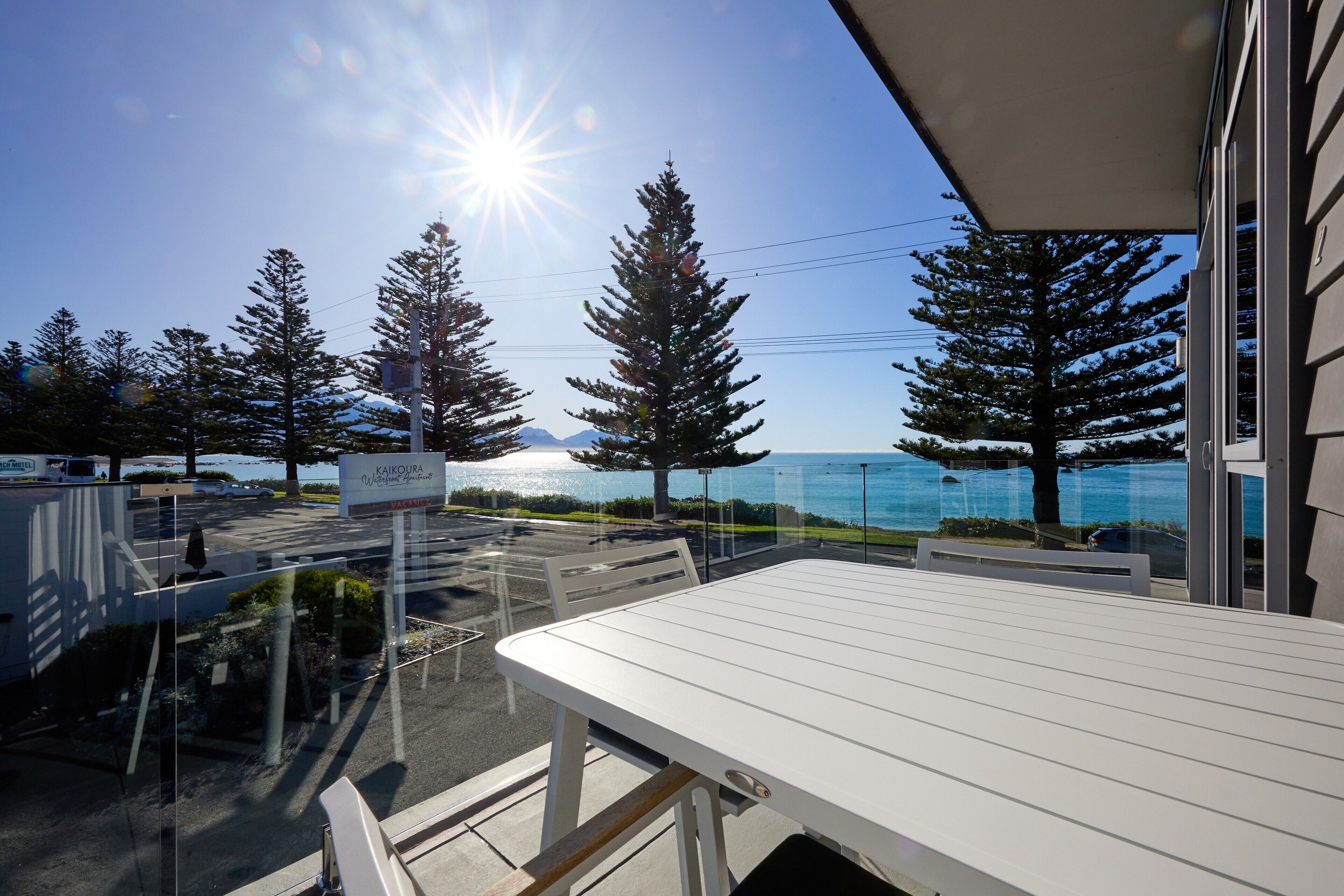 A balcony with a view of the sea, trees, and a sign for 'Kaikoura'.