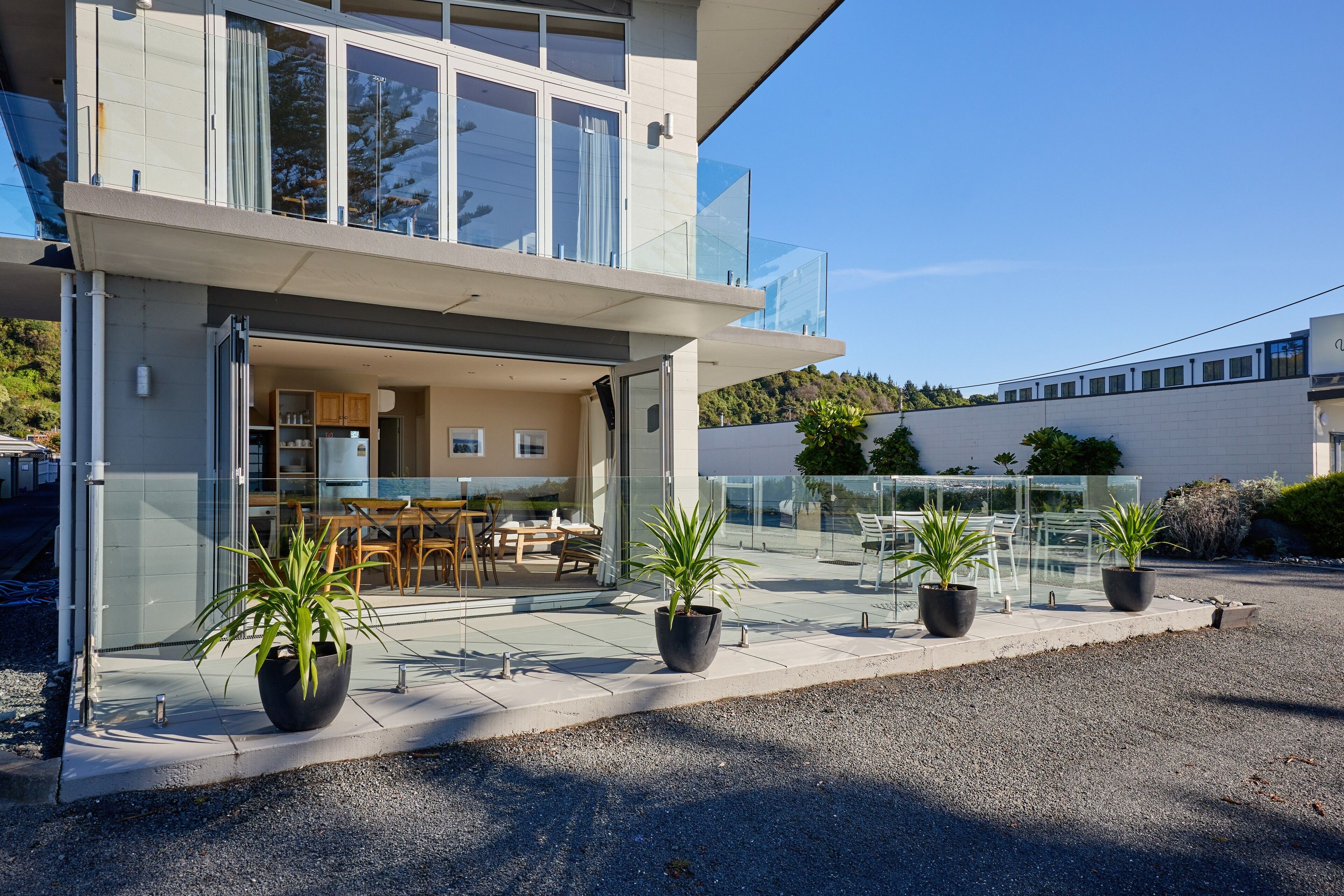 Ein modernes, zweistöckiges Haus mit einem Glasbalkon, einer sichtbaren Küche und Kübelpflanzen.