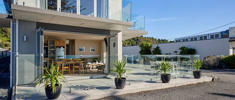 Ein modernes, zweistöckiges Haus mit einem Glasbalkon, einer sichtbaren Küche und Kübelpflanzen.
