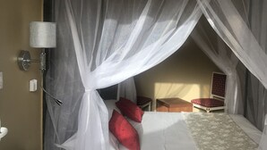A bedroom with a canopy bed, a bedside table, a lamp, and a small bedside table with a red cushion. - Chez Daniel mbene (Mbour)