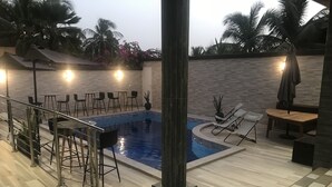 An indoor swimming pool area with a tiled floor, lounge chairs, and a bar area with stools. - Chez Daniel mbene (Mbour)