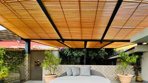 Un espacio de estar al aire libre con forma circular y diseño tejido, rodeado de plantas en macetas y una pared con diseño.