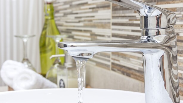 Un baño con un grifo cromado moderno, una botella de vidrio y una toalla.
