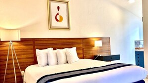 Habitación de hotel con una cama grande, cabecera de madera, mesita de noche con lámpara y un cuadro enmarcado en la pared.