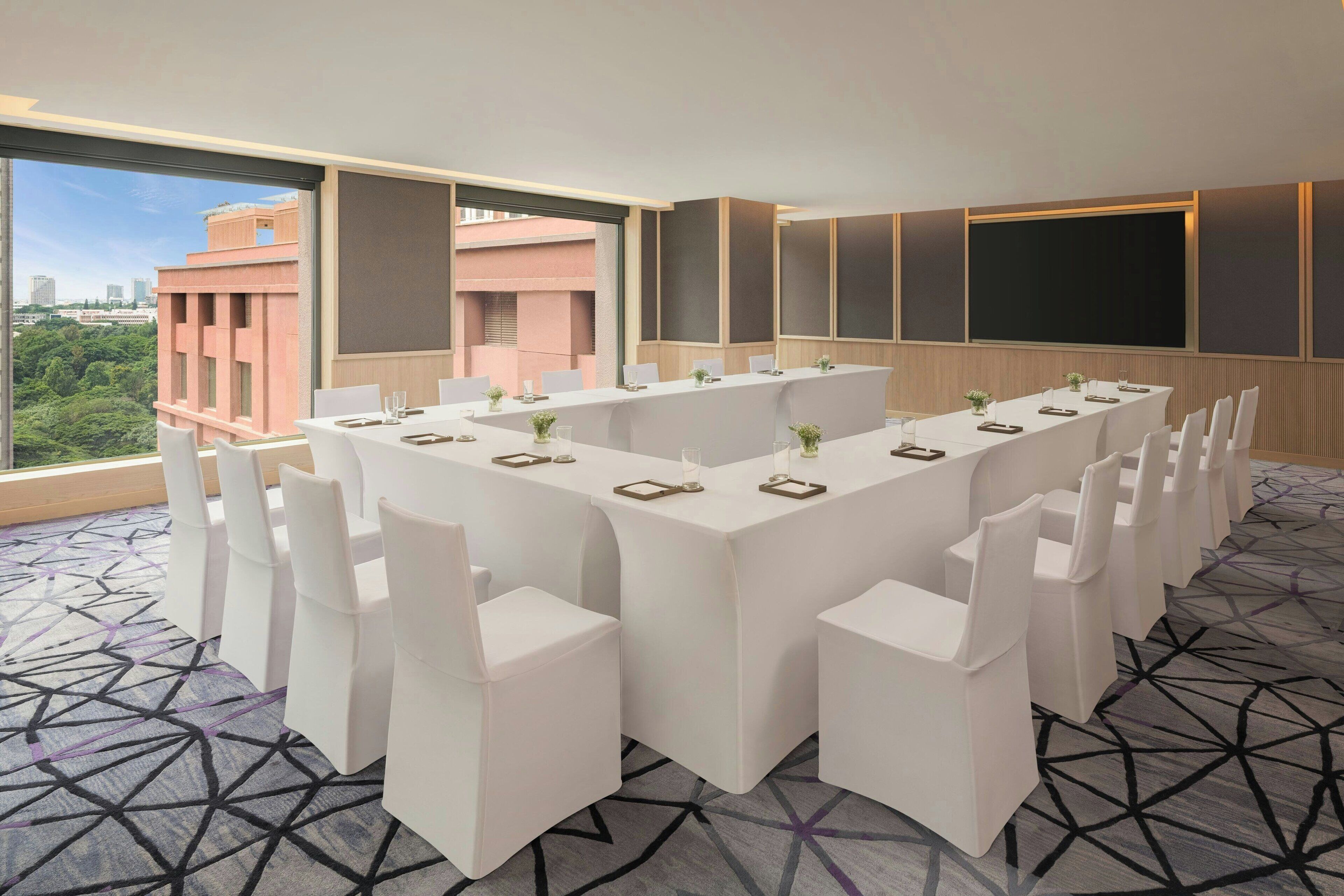 Un salón de conferencias con una larga mesa, sillas blancas y vistas a la ciudad a través de amplios ventanales.