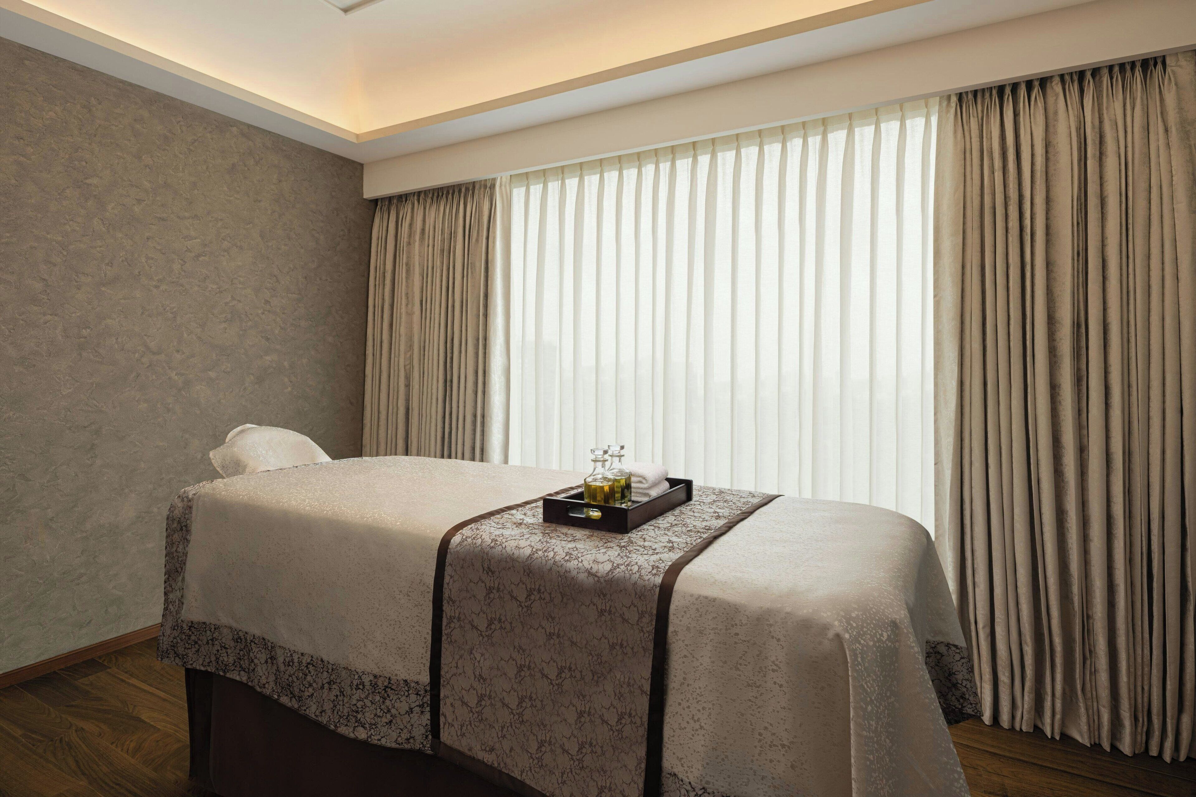 A neatly made bed with a tray of toiletries, a pillow, and a window with curtains.