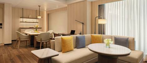 A modern hotel room with a sofa, a dining table, and a laptop.