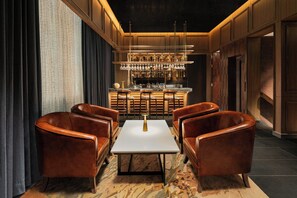 A bar area with leather chairs, a central table, and a bar counter with hanging glasses.