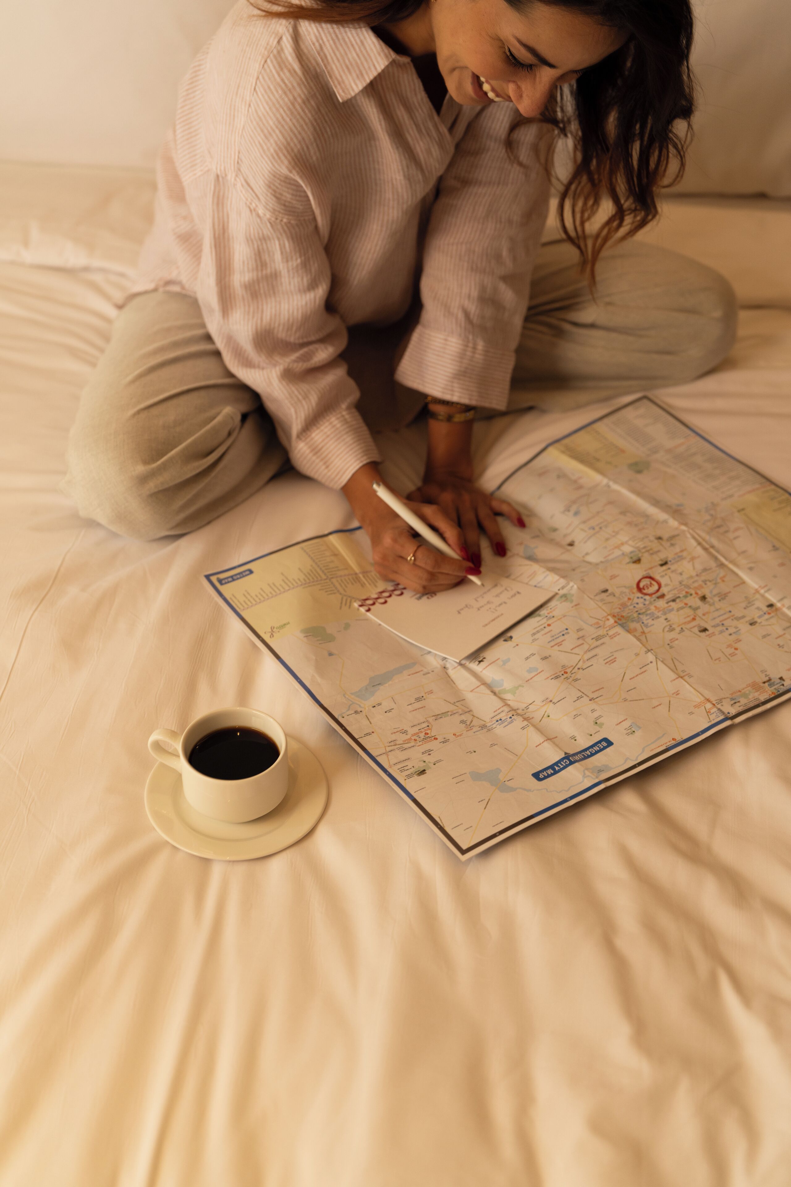 A person sitting on a bed with a map and a cup of coffee.