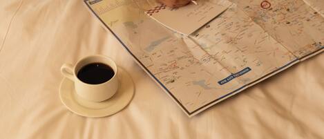 A person sitting on a bed with a map and a cup of coffee.