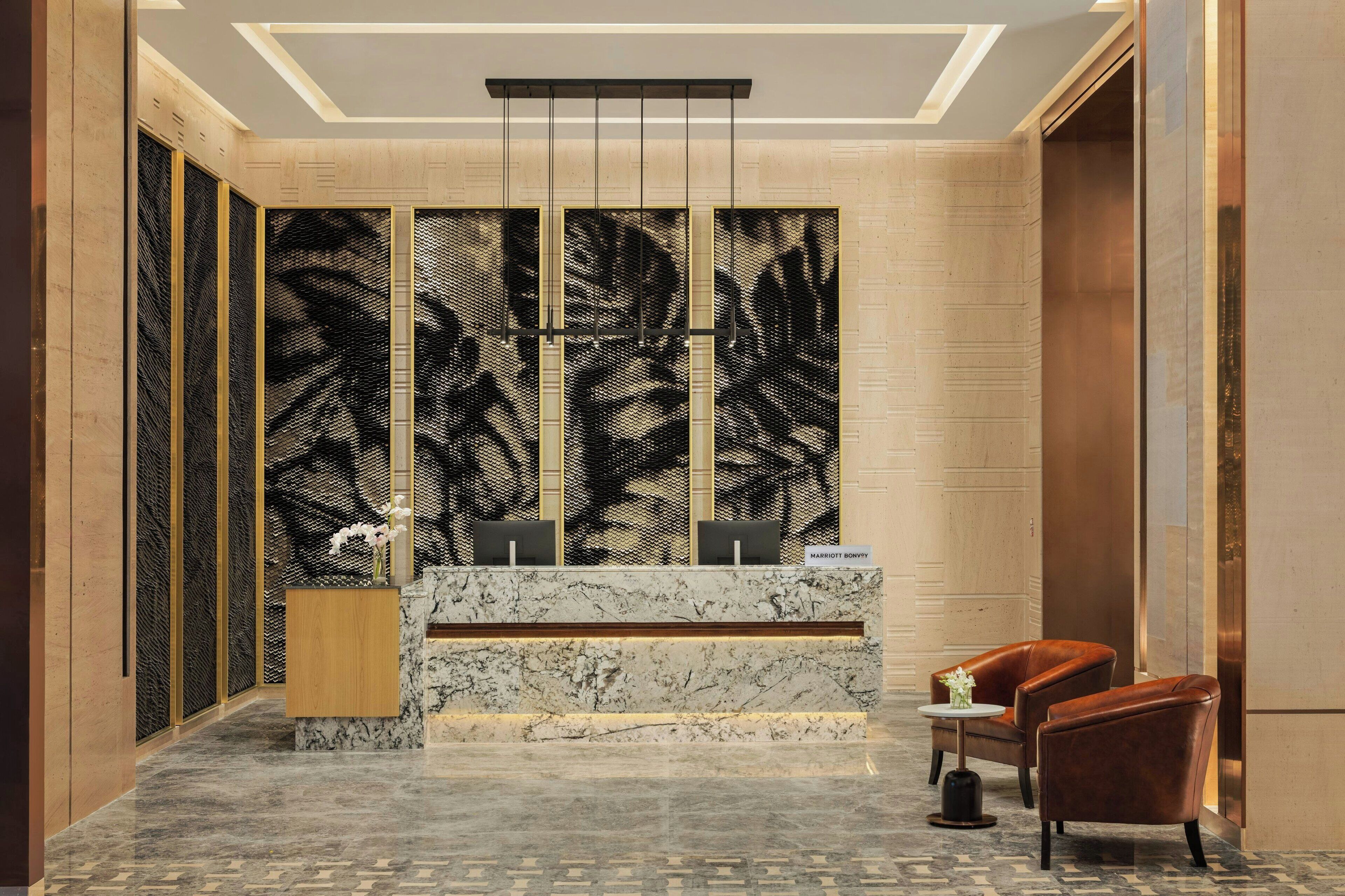 Un vestíbulo con un mostrador de recepción, dos sillones de cuero, una pequeña mesa con un jarrón de flores y una pared con una gran obra de arte abstracta.