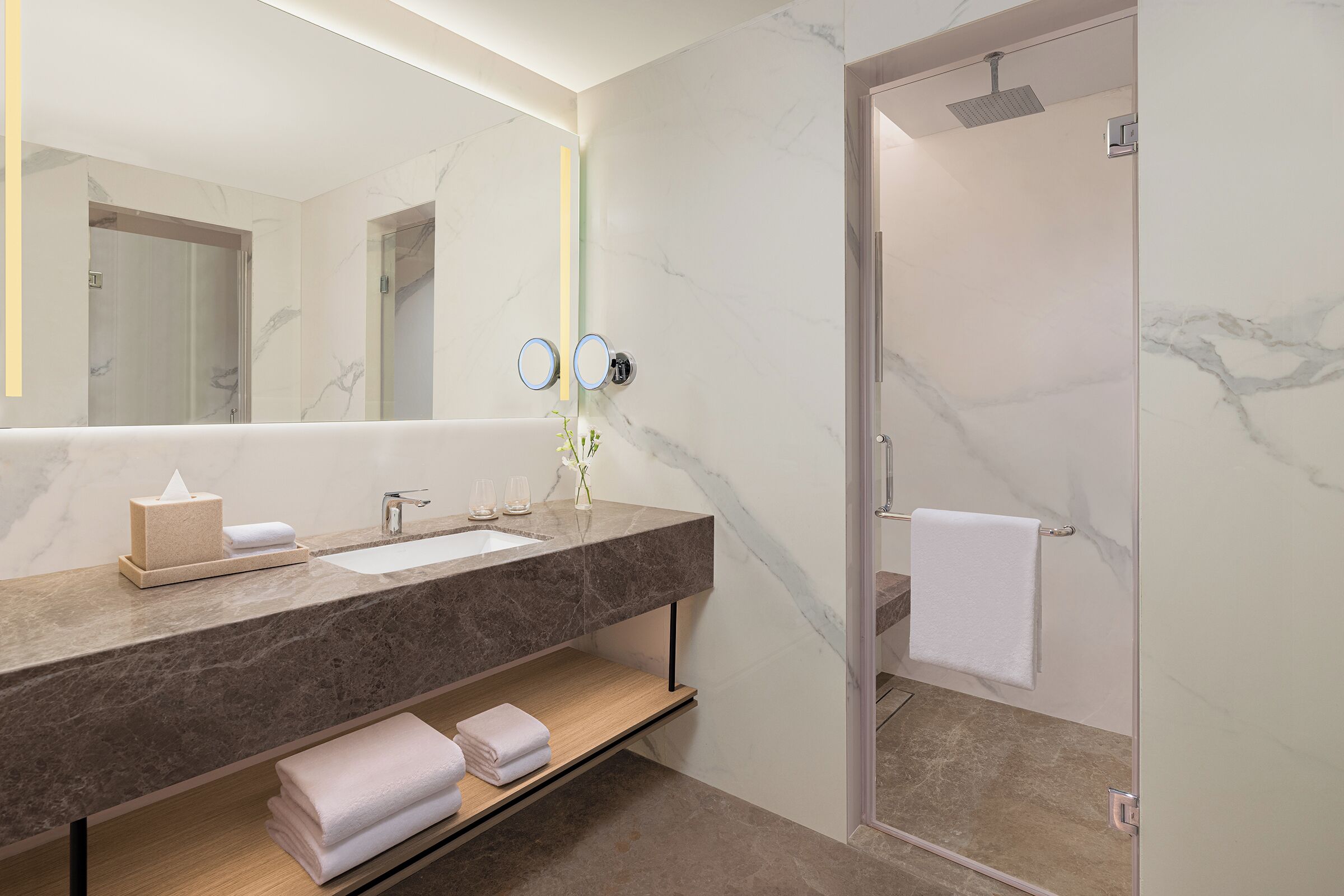 Un baño moderno con tocador de mármol, ducha con cerramiento de vidrio y un perchero para toallas.