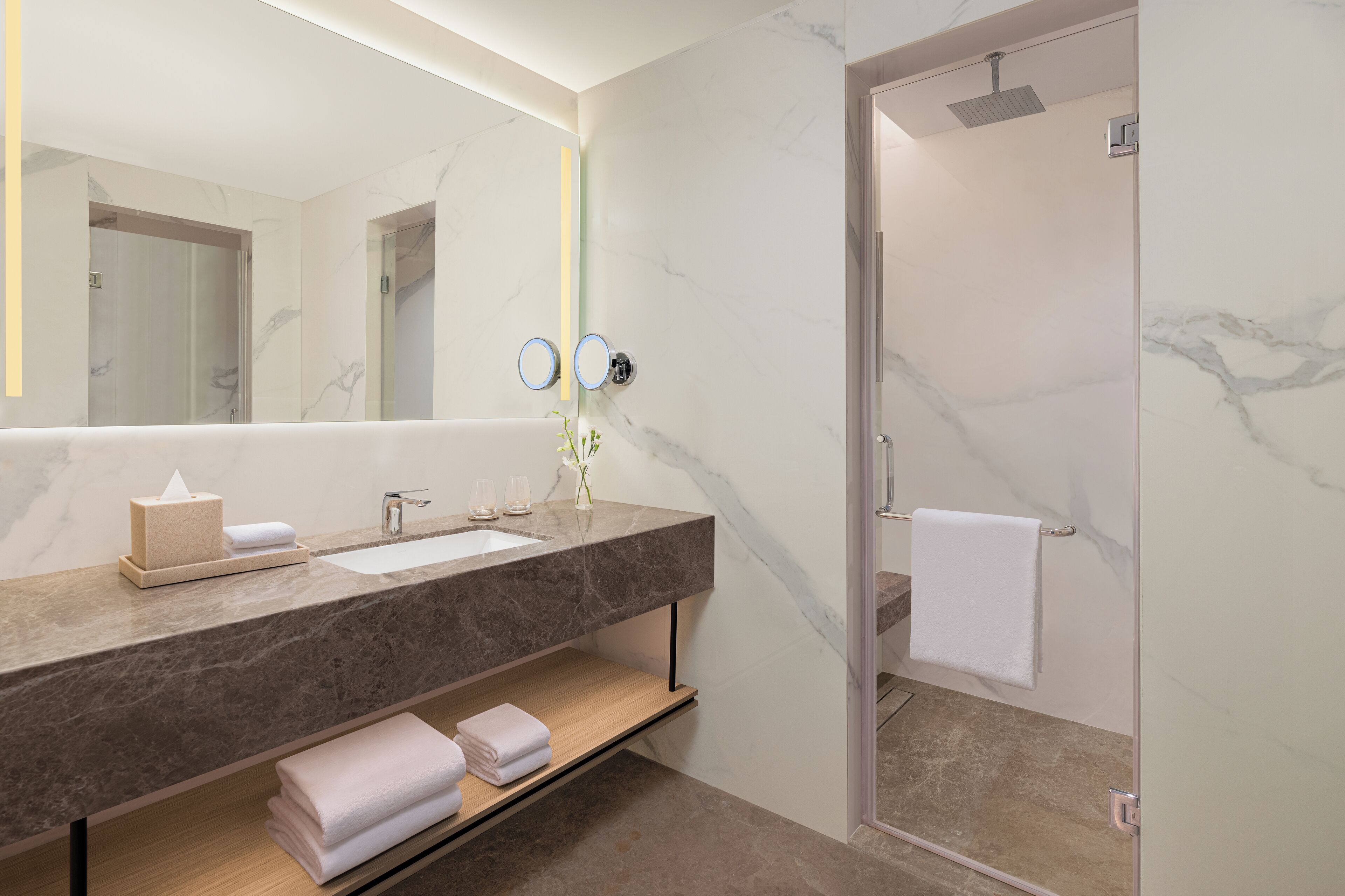A modern bathroom with a marble countertop, a large mirror, a towel rack, and a shower area.
