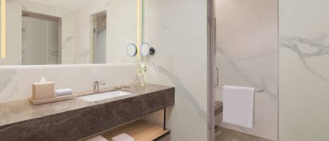 A modern bathroom with a marble countertop, a large mirror, a towel rack, and a shower area.