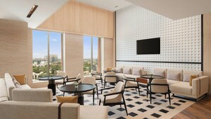 A modern living room with a large window, a flat-screen TV mounted on a textured wall, and a mix of sofas and chairs arranged around a central coffee table.