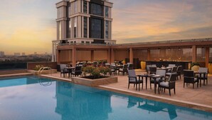 Un área de piscina en la azotea con vistas al horizonte urbano, mobiliario exterior y una estructura de edificio moderna.