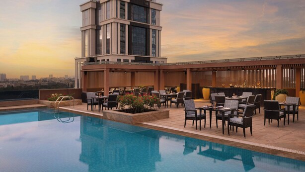 Un área de piscina en la azotea con vistas al horizonte urbano, mobiliario exterior y una estructura de edificio moderna.