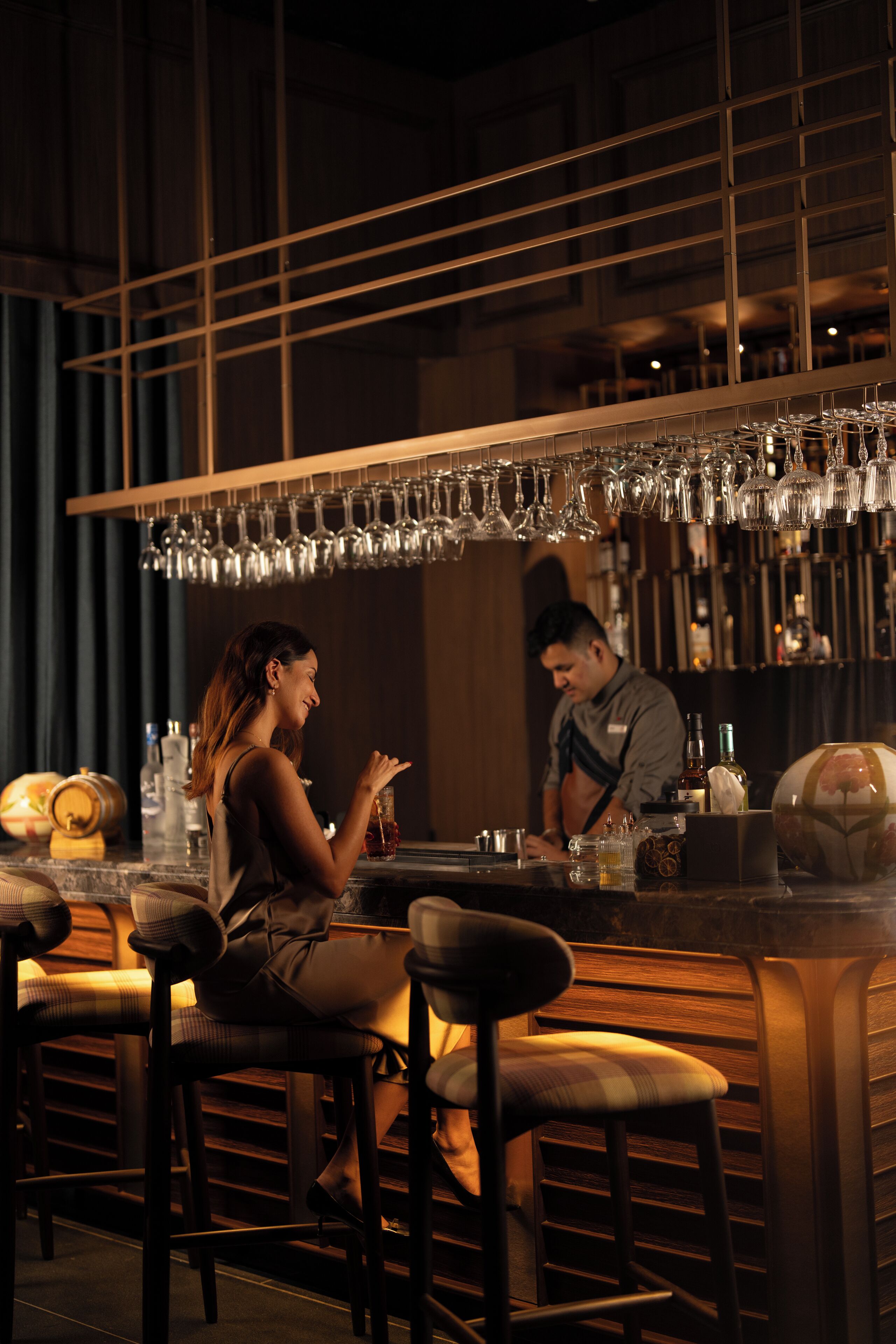 A bar area with stools and a bar counter, glasses hanging above, and a bartender at work.