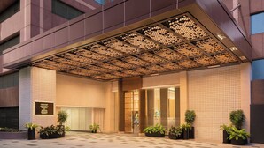 Una entrada de hotel moderna con un dosel de diseño geométrico, piso a cuadros y plantas en macetas.