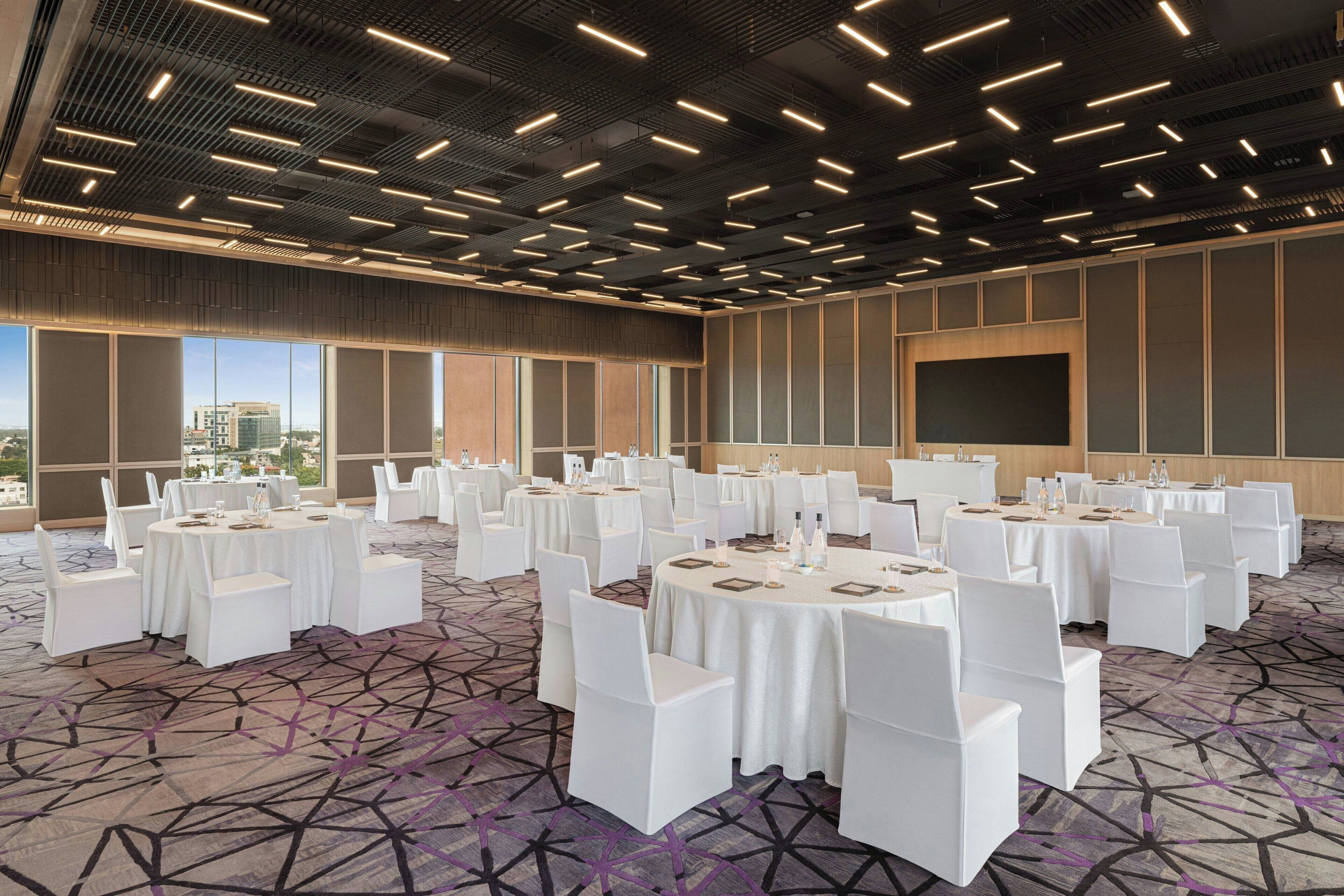 Une salle de conférence dotée de plusieurs tables rondes, de chaises blanches et d’un tapis à motifs.