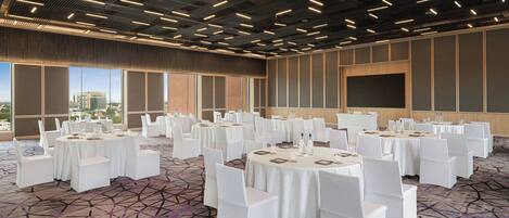 Une salle de conférence dotée de plusieurs tables rondes, de chaises blanches et d’un tapis à motifs.