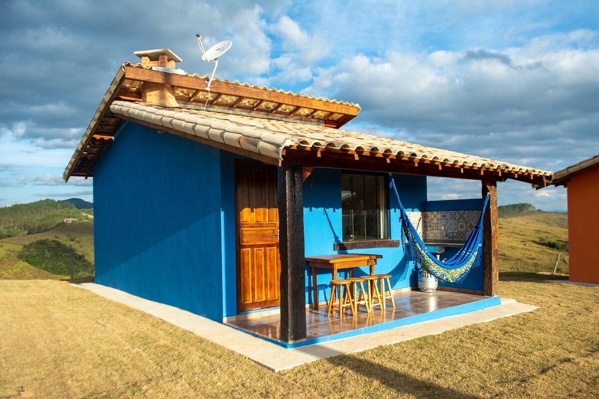 A small, blue house with a tiled roof, a wooden door, and a patio area with a table and chairs.
