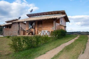 A rustic brick house with a tiled roof, a wooden door, and a small patio with white plastic chairs. - Estalagem Mirante do Sol (Lima Duarte)