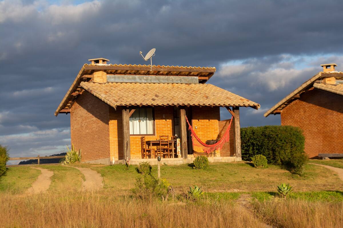 A rustic brick house with a tiled roof, a hammock, and a satellite dish.