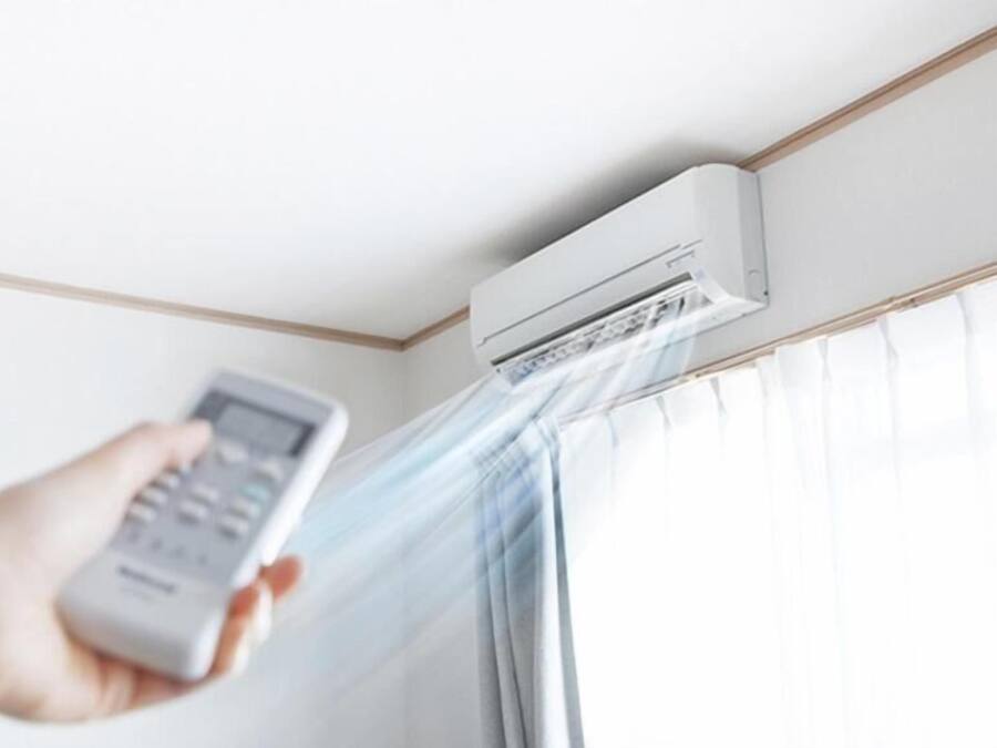 Una mano sosteniendo un control remoto cerca de un equipo de aire acondicionado instalado en la pared.