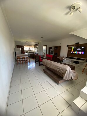 Een woonkamer met een bank, televisie en een keuken op de achtergrond.