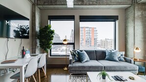 A modern living room with a grey sofa, a white coffee table, and a TV displaying 'MINNESOTA'. - MINNeSTAY* Sable 401 - Studio | North Loop | Target Center (Minneapolis)