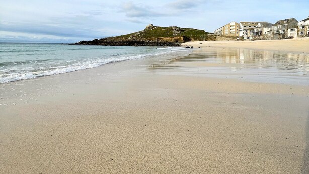 Una playa con un promontorio rocoso y edificios al fondo.