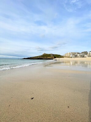 A beach with a rocky outcrop and buildings in the background. - ST ANNAS COTTAGE - wonderful family seaside cottage next to Porthmeor beach (St Ives)