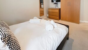 Un dormitorio con cama, armario de madera, televisor, espejo y cuadros en la pared.