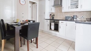 Una cocina moderna con armarios blancos, una mesa de comedor con sillas y un reloj en la pared.