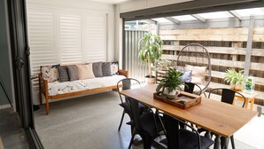 A cozy room with a wooden dining table, black chairs, a sofa with cushions, and a large window with blinds.