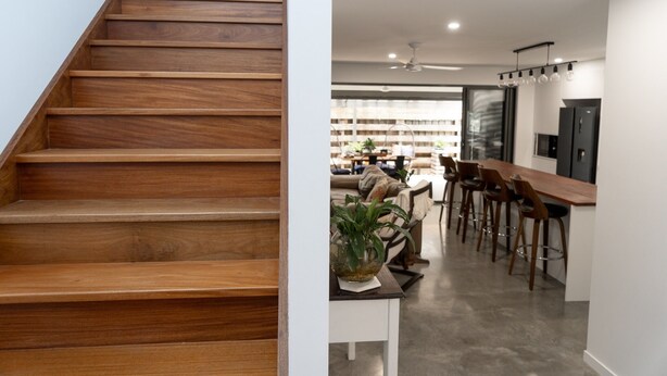 A wooden staircase leading to a modern kitchen with bar seating.