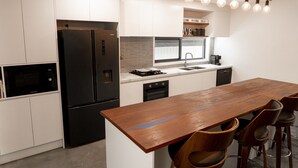 A modern kitchen with white cabinetry, a black refrigerator, a built-in oven, a wooden dining table with four chairs, and a hanging light fixture.