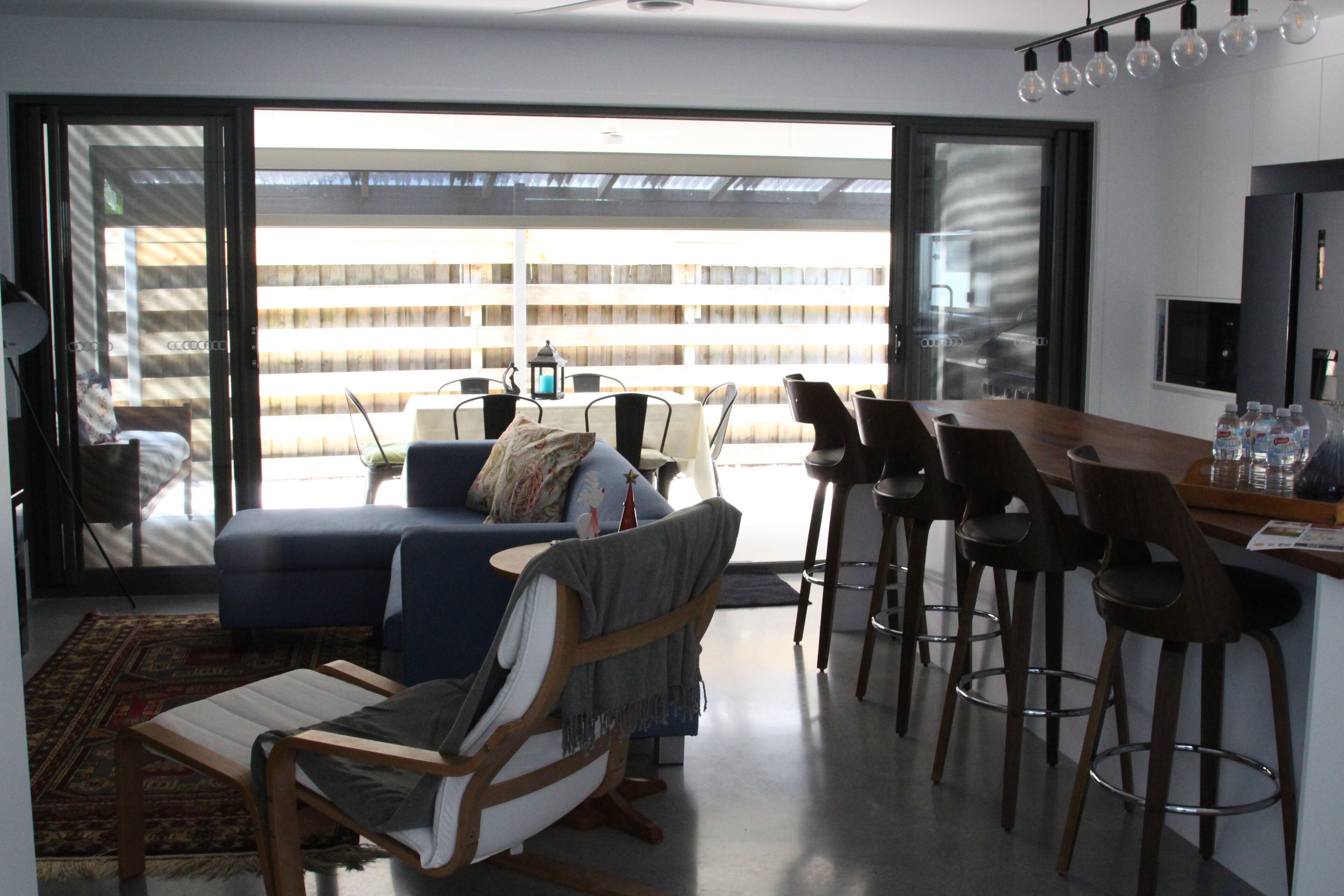 A modern living room with a sofa, a rocking chair, and a dining area with bar stools.