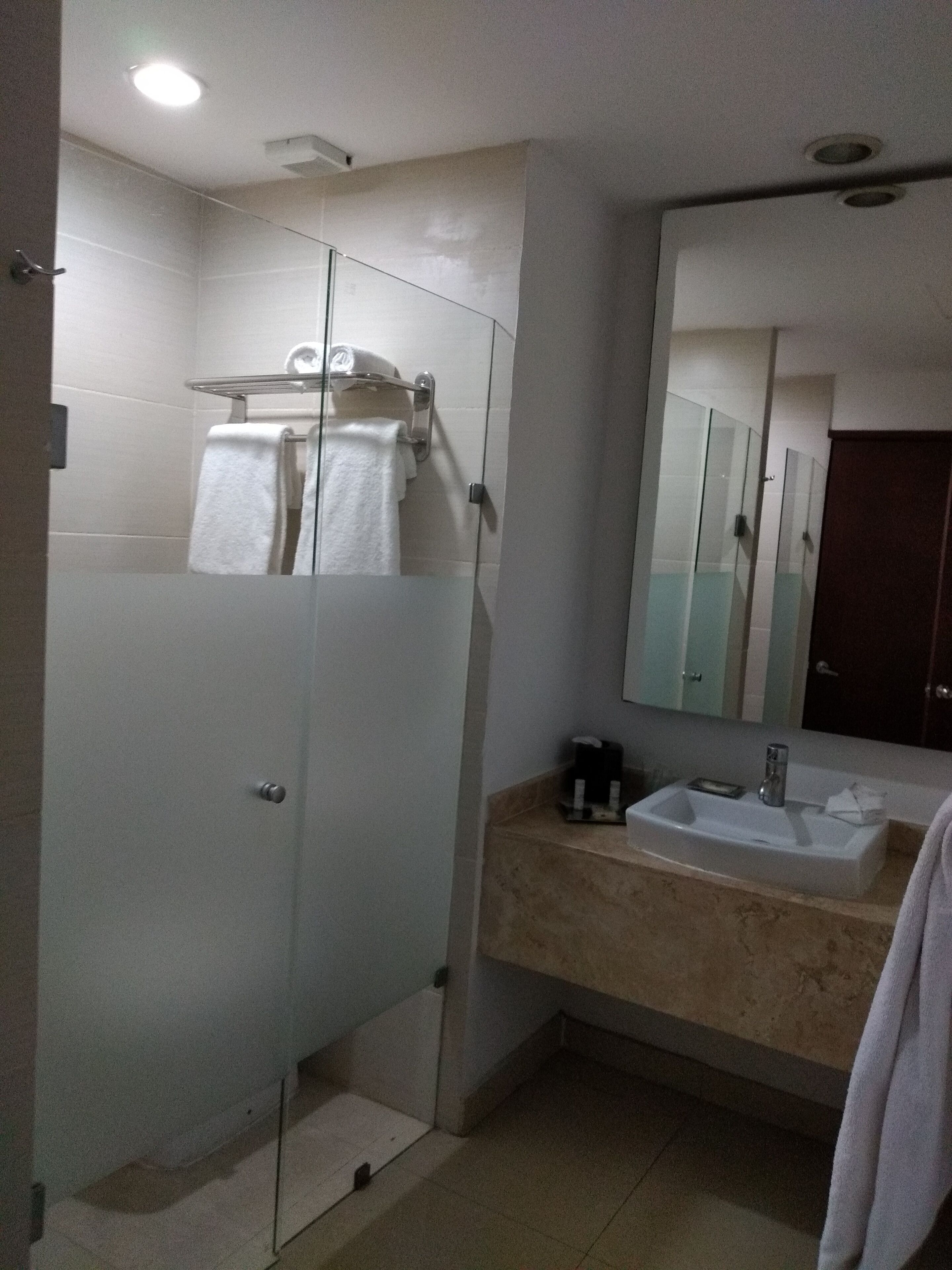 Un baño moderno con ducha envuelta en vidrio, un lavabo blanco con un espejo encima y un perchero para toallas.