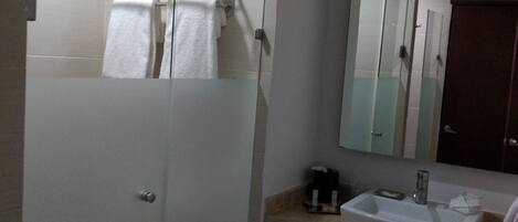 A modern bathroom with a glass-enclosed shower, a white sink with a mirror above it, and a towel rack.