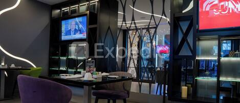 A modern interior with a dining area, a television displaying a news channel, and a bar area with decorative lighting.
