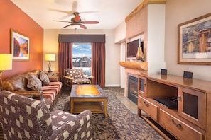A hotel room with a sofa, armchair, and a television on a wooden cabinet.