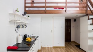 A compact kitchen with a wooden loft, white cabinetry, and a black countertop. - R&R Apart Cracow (Kraków)