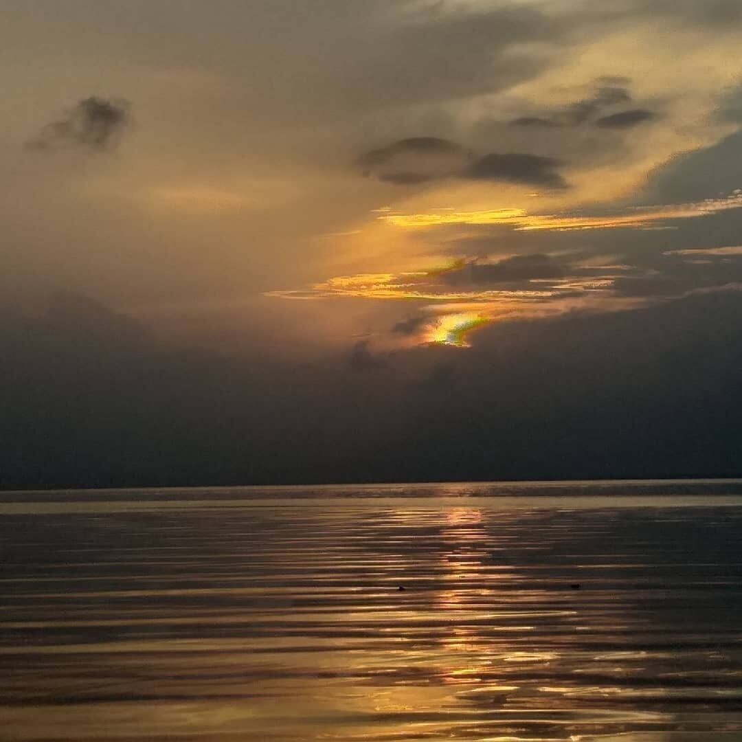 Ein Sonnenuntergang über ruhigem Wasser, das Licht spiegelt sich in den Wolken.